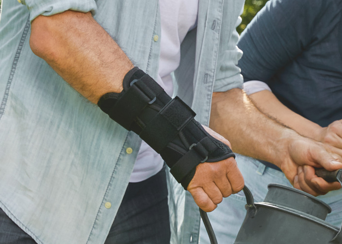 Uomo che usa lo stabilizzatore da polso Actimove Sports Edition mentre annaffia il giardino a causa di lesioni. Uomo che usa lo stabilizzatore da polso Actimove Sports Edition mentre annaffia il giardino a causa di lesioni.